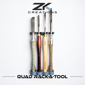 May include: A grey plastic wall-mounted rack holding four woodturning chisels with varied handles. The rack features the text ZK CREATIONS at the top and QUAD RACK-A-TOOL at the bottom. The tools include metal blades and wooden or textured handles.