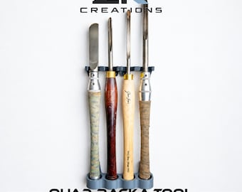 May include: A grey plastic wall-mounted rack holding four woodturning chisels with varied handles. The rack features the text ZK CREATIONS at the top and QUAD RACK-A-TOOL at the bottom. The tools include metal blades and wooden or textured handles.