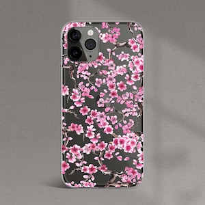 May include: A clear phone case with a pink and white floral design. The case features a pattern of cherry blossoms on a black background.