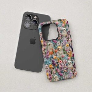 May include: A dark gray smartphone next to a phone case with a floral and skeleton design. The case features a colorful pattern of flowers and small skeletons.