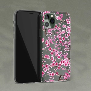 Puede incluir: Una funda transparente para tel&eacute;fono con un dise&ntilde;o floral que presenta flores de cerezo rosas sobre un fondo gris. La funda est&aacute; dise&ntilde;ada para un iPhone con una c&aacute;mara de triple lente.