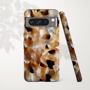 May include: A phone case with a mosaic design in shades of brown, tan, and white. The case is shown upright and leaning against another case with the same design. The phone case has a camera cutout and button details.