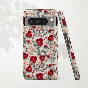 Może przedstawiać: Białe etui na telefon z czerwonym haftem kwiatowym. Etui ma wycięcie na obiektyw aparatu.