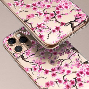 Puede incluir: Una funda transparente para tel&eacute;fono con un dise&ntilde;o floral con flores de cerezo rosas sobre un fondo dorado. La funda est&aacute; dise&ntilde;ada para un iPhone con una c&aacute;mara de triple lente.