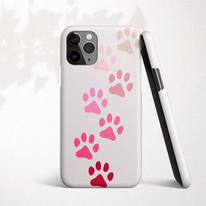 Könnte beinhalten: Eine weiße iPhone-Hülle mit einem pinkfarbenen und roten Pfotenabdruck-Design. Die Hülle hat ein klares Kameraobjektiv.