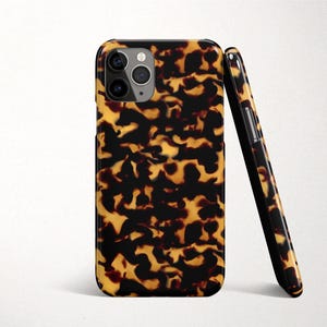 May include: Two phone cases with a tortoiseshell design. The cases are mainly black and amber with a glossy finish. One case is upright, and the other is leaning against it.