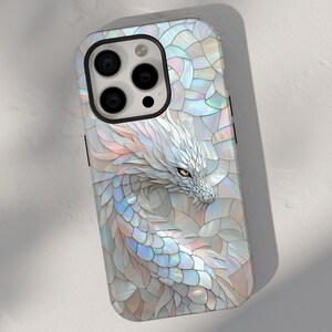 Può includere: Una custodia per iPhone bianca con un design a drago realizzato con tessere di mosaico iridescenti. La testa del drago è visibile nell'angolo in alto a destra della custodia.