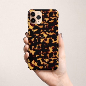 May include: A black phone case with a brown and black tortoiseshell pattern. The case has a camera lens cutout.