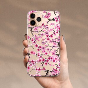 Puede incluir: Una funda transparente para tel&eacute;fono con un dise&ntilde;o de flores de cerezo rosa y negro. La funda est&aacute; dise&ntilde;ada para un iPhone.