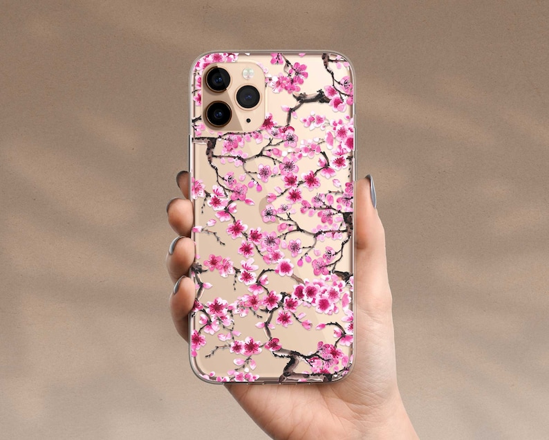 Puede incluir: Una funda transparente para tel&eacute;fono con un dise&ntilde;o de flores de cerezo rosa y negro. La funda est&aacute; dise&ntilde;ada para un iPhone.