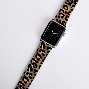 Puede incluir: Una correa de reloj de estampado de leopardo negro y dorado para un Apple Watch.