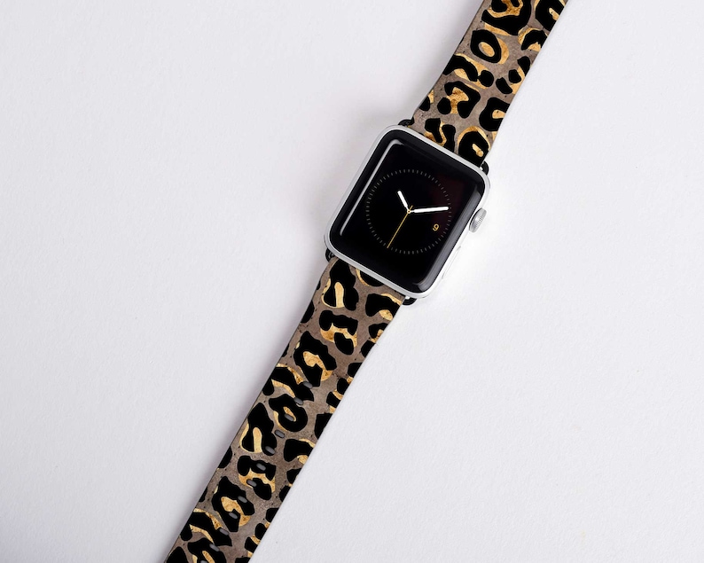 Puede incluir: Una correa de reloj de estampado de leopardo negro y dorado para un Apple Watch.