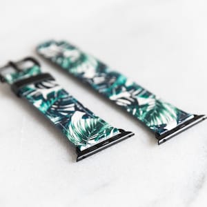 Puede incluir: Dos correas de reloj negras y blancas con un patr&oacute;n de hojas tropicales. Las correas son de cuero y tienen una hebilla de metal negro.