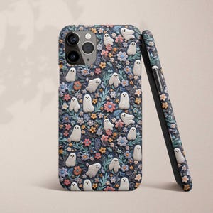 May include: A phone case with a dark blue background and a pattern of white ghosts and colorful flowers. The case has a cutout for the camera lens.