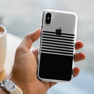 K&ouml;nnte beinhalten: Eine transparente Handyh&uuml;lle mit einem schwarz-wei&szlig;en Streifenmuster und einem schwarzen Apple-Logo. Die H&uuml;lle befindet sich auf einem schwarzen Hintergrund.