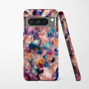 May include: A colorful phone case with a unique, abstract design. The case features a mix of pink, blue, green, and yellow fragments, creating a mosaic-like pattern. The phone case is shown upright and leaning against another case, showcasing the design.