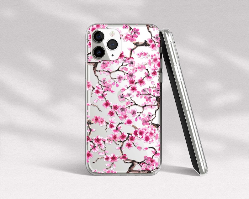 Puede incluir: Una funda transparente para tel&eacute;fono con un dise&ntilde;o de flores de cerezo rosa y blanco. La funda est&aacute; dise&ntilde;ada para un iPhone.