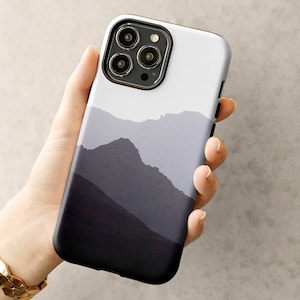 Könnte beinhalten: Eine schwarze Handyhülle mit einem weißen und grauen Berglandschaft-Design. Die Hülle hat einen Kameraausschnitt mit vier schwarzen Linsen.