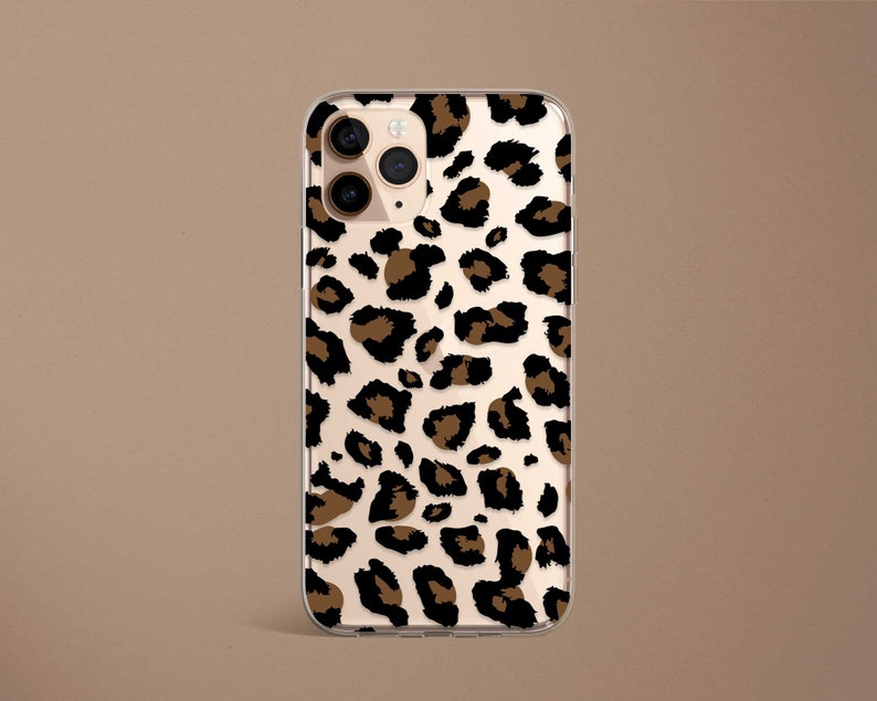 May include: A clear phone case with a brown and black leopard print design. The case has a cutout for the phone's camera.