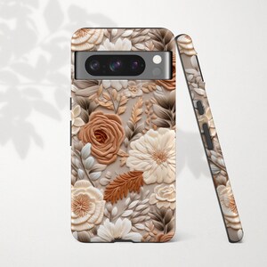 May include: A phone case with a floral design in shades of beige, brown, and white. The case features a raised, textured pattern of roses, leaves, and other botanical elements. A second case is leaning against the first, showing the same design.