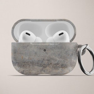 May include: A gray concrete case with a metal ring for carrying AirPods. The case has a textured surface and is open to reveal two white AirPods.