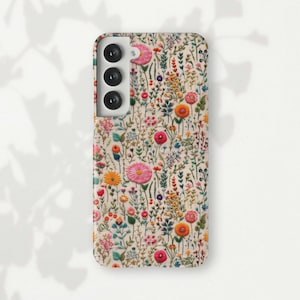 Könnte beinhalten: Eine weiße Handyhülle mit einem Blumenmuster. Die Hülle hat eine erhöhte Kameraabdeckung mit drei Objektiven.