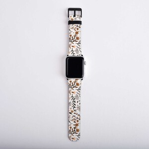 May include: A white Apple Watch band with a floral pattern in shades of brown and beige.