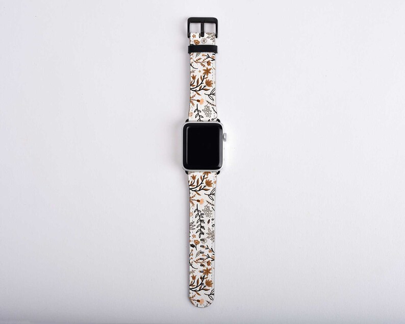 May include: A white Apple Watch band with a floral pattern in shades of brown and beige.