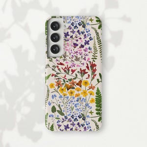 May include: A white phone case with a floral design featuring pressed flowers in shades of pink, purple, yellow, and green. The case has a cutout for the camera lens.