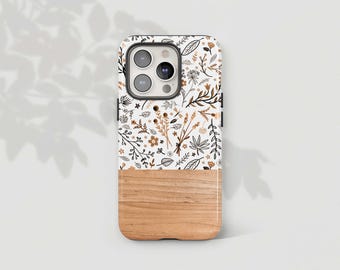 Puede incluir: Una funda de teléfono blanca con un patrón floral y un diseño de veta de madera en la mitad inferior. La funda tiene un recorte para la cámara y un borde negro.