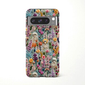 May include: A phone case featuring a colorful floral design with small skeleton figures. The case has a variety of flowers in shades of pink, yellow, blue, and purple. The skeletons are white and beige.