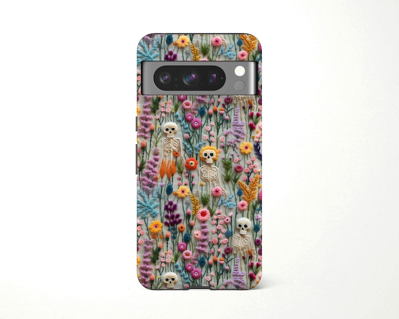 May include: A phone case featuring a colorful floral design with small skeleton figures. The case has a variety of flowers in shades of pink, yellow, blue, and purple. The skeletons are white and beige.
