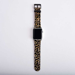 Puede incluir: Una correa de reloj de leopardo negro y dorado para un Apple Watch.