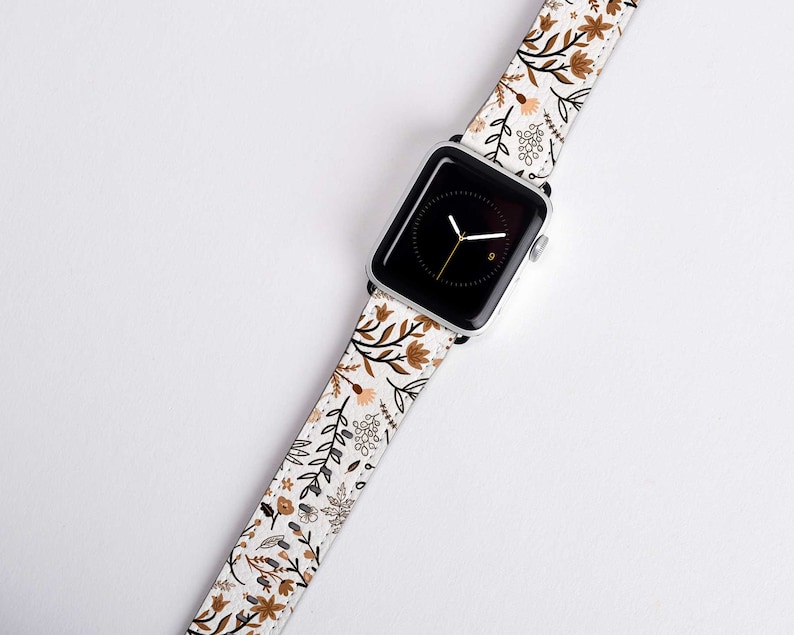 May include: A white Apple Watch band with a floral pattern in brown and beige. The band has a white background with brown and beige flowers and leaves.