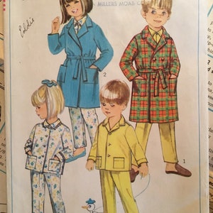 May include: A vintage Simplicity sewing pattern for children's pajamas. The pattern includes three different styles: a blue robe, a plaid robe, and a yellow pajama set. The pattern number is 7407 and the size is 2.