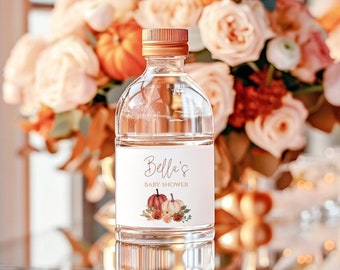 May include: A clear plastic water bottle with a gold lid and a white label that says "Bella's Baby Shower" with a watercolor illustration of pumpkins and flowers.