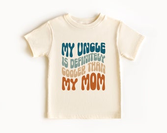 May include: A cream colored t-shirt with the text "My Uncle is definitely cooler than My Mom" in a retro font with blue, green, and orange colors.