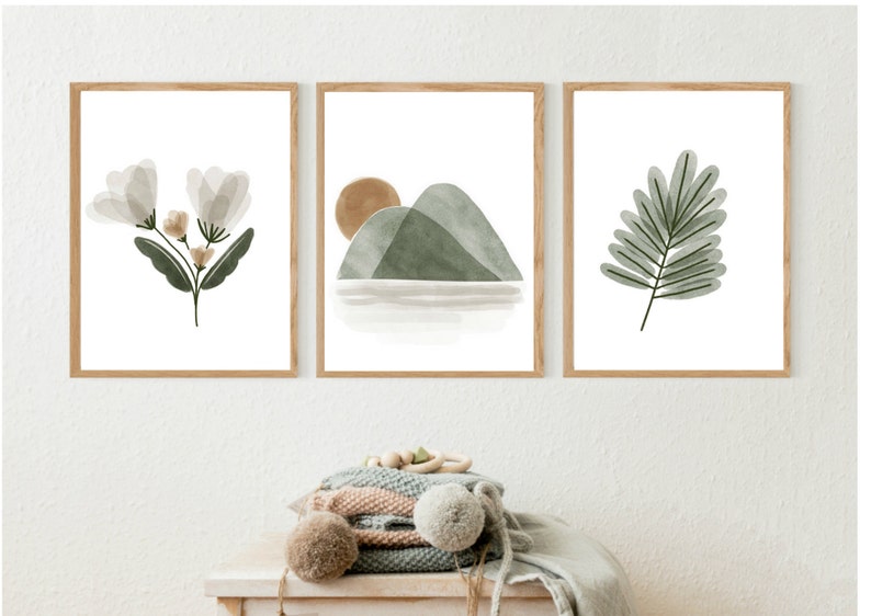 May include: Set of three minimalist watercolor prints featuring a green leaf, a mountain landscape with a sun, and a bouquet of white flowers. The prints are framed in natural wood frames.
