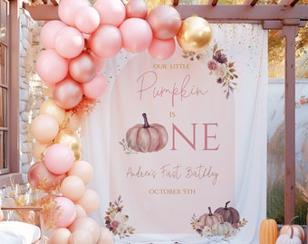 Op de afbeelding: Een roze en gouden achtergrond met een pompoenthema voor een eerste verjaardag. De achtergrond heeft de tekst "Our Little Pumpkin is One" en "Andrea's First Birthday, October 5th".