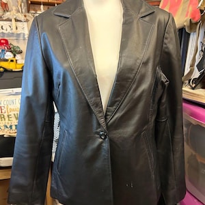 Könnte beinhalten: Ein schwarzer Lederblazer mit einem Knopfverschluss und einem Schalkragen.
