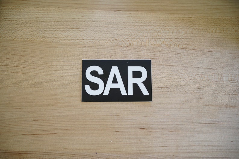 Puede incluir: Una pegatina rectangular negra con la palabra "SAR" en letras blancas.
