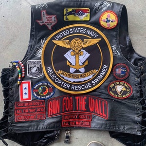 May include: A black leather vest with various patches, including a United States Navy helicopter rescue swimmer patch, a Run for the Wall patch, and a Southern Route patch. The vest has a lace-up back and is decorated with beaded strings.