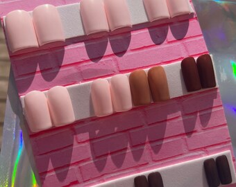 May include: A set of press-on nails in three different colors: pink, brown, and dark brown. The nails are arranged on a pink and white display card with the text "Candymunaiz" printed on it.