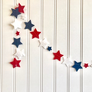 May include: A red, white, and blue felt star garland. The garland is made of felt stars in various sizes and is strung together with white thread.