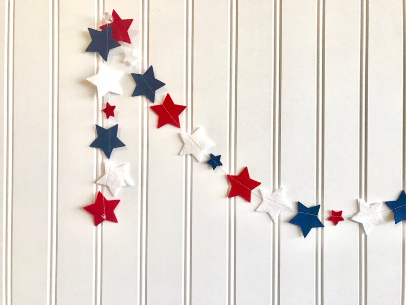 May include: A red, white, and blue felt star garland. The garland is made of felt stars in various sizes and is strung together with white thread.