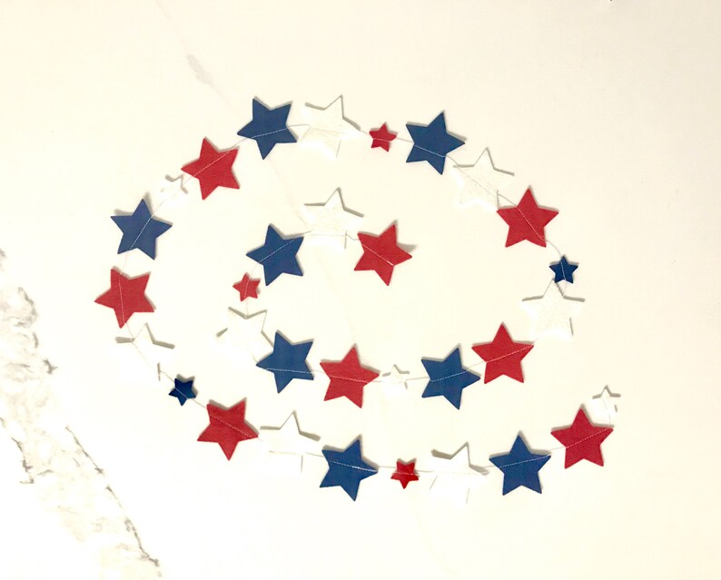May include: A red, white, and blue star garland with alternating colors. The garland is made of paper stars and is strung together with white thread.