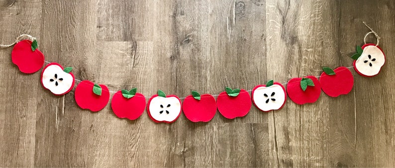 May include: A red felt apple garland with green leaves and white felt apple slices. The garland is strung on twine and is perfect for a fall or autumn themed party.