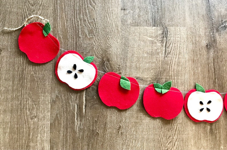 May include: A felt apple garland with red apples and white apple slices with black seeds. The garland is strung with twine and has green felt leaves.