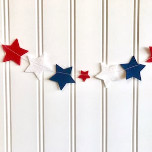 May include: A red, white, and blue felt star garland. The garland is made of felt stars in red, white, and blue, and is strung together with white thread.