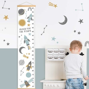 May include: A height chart with a space theme, featuring rockets, planets, stars, and the text "Reach for the Stars." The chart is white with a wooden frame and measures up to 160 inches. Decorative wall stickers of stars and planets are also visible.